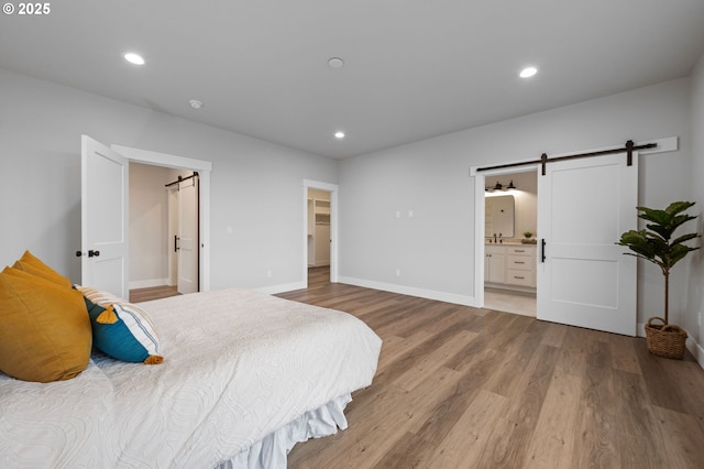 bedroom with a barn door, a spacious closet, wood finished floors, and recessed lighting