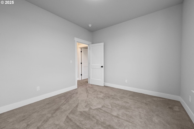 spare room with baseboards and light colored carpet