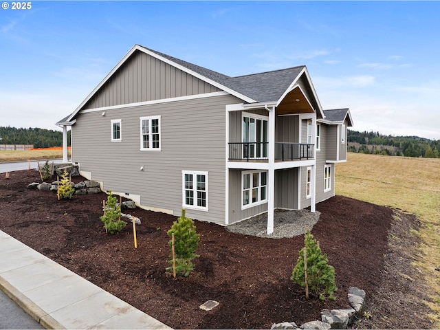 view of side of property with board and batten siding, roof with shingles, and a balcony