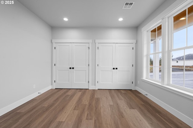 unfurnished bedroom featuring baseboards, wood finished floors, visible vents, and multiple closets