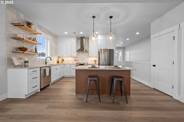 kitchen with white cabinets, wall chimney exhaust hood, appliances with stainless steel finishes, a center island, and open shelves