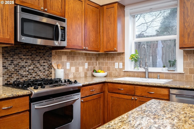 kitchen featuring stainless steel appliances, light stone countertops, sink, and backsplash