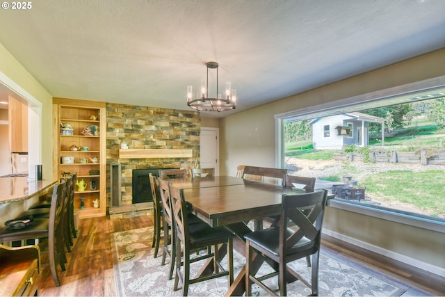 dining space with built in features, wood finished floors, baseboards, an inviting chandelier, and a stone fireplace