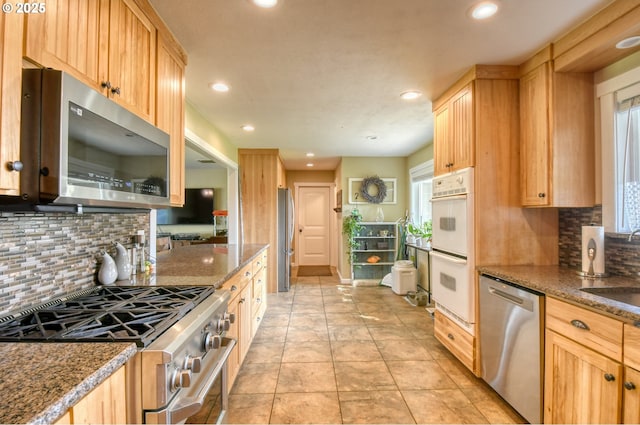 kitchen with dark stone countertops, stainless steel appliances, light brown cabinetry, and recessed lighting