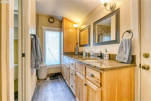 bathroom featuring vanity, lofted ceiling, wood finished floors, and baseboards