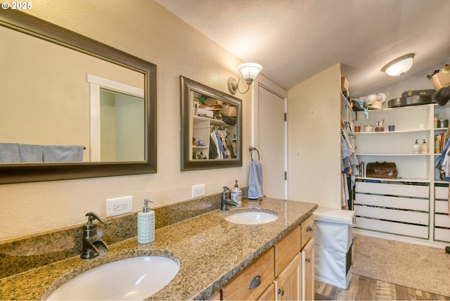 bathroom with double vanity, wood finished floors, lofted ceiling, and a sink