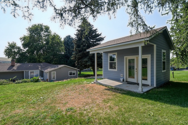 back of property with an outdoor structure, a lawn, french doors, and a patio