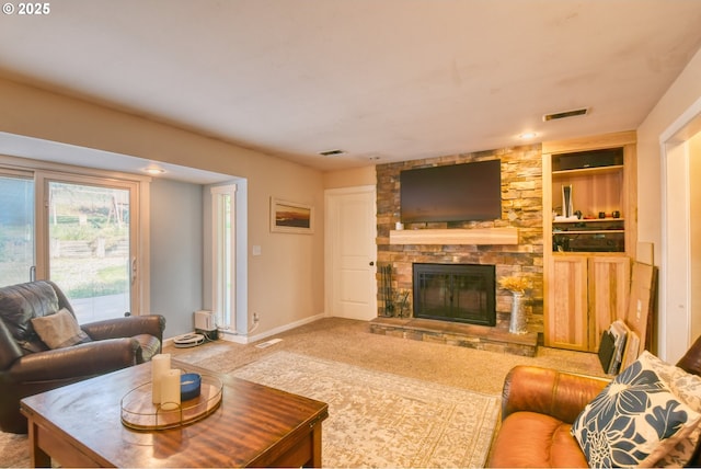 carpeted living room featuring visible vents, built in shelves, a stone fireplace, and baseboards