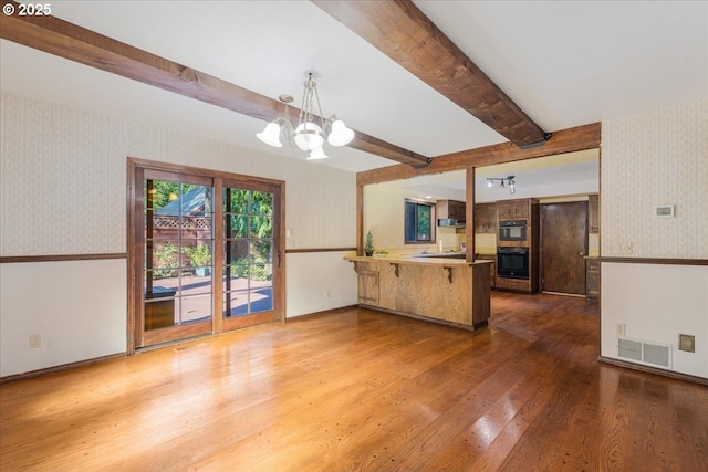 65257 E Sandy River Ln, Rhododendron, OR 97049 - kitchen featuring wallpapered walls, black oven, a peninsula, wood finished floors, and a chandelier