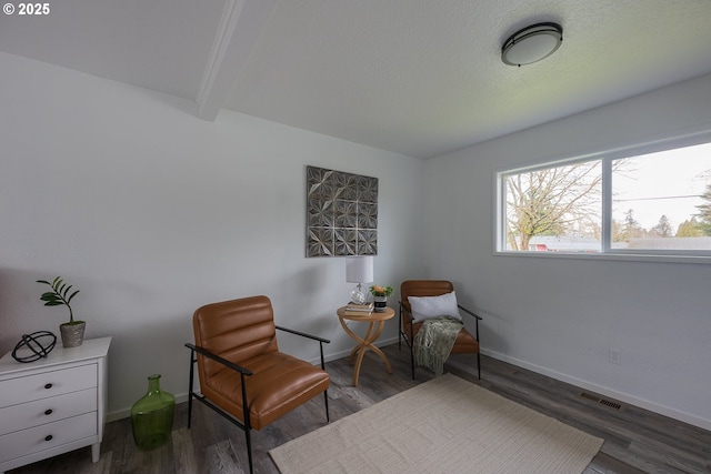 living area with visible vents, beam ceiling, baseboards, and wood finished floors