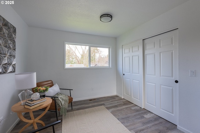 sitting room with visible vents, a textured ceiling, baseboards, and wood finished floors