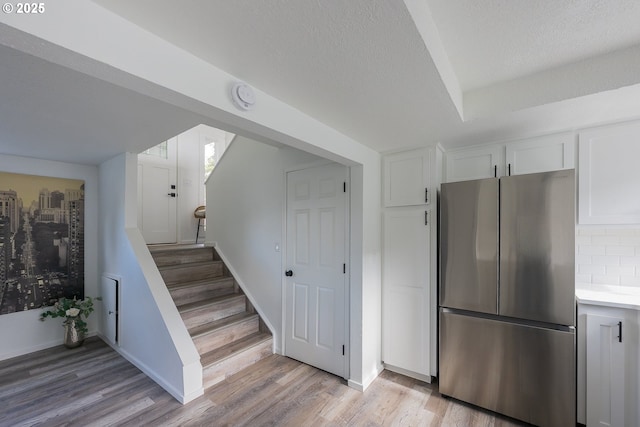 interior space with light countertops, backsplash, light wood-style floors, freestanding refrigerator, and white cabinets