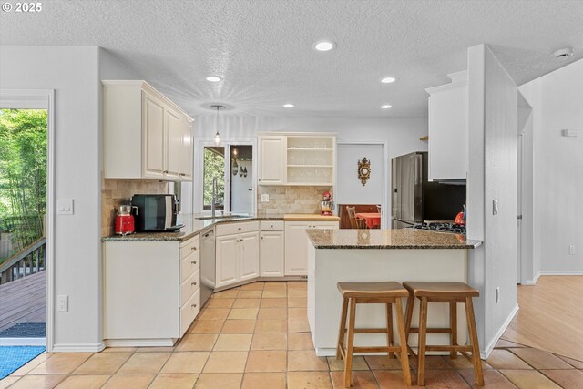 kitchen with open shelves, a sink, tasteful backsplash, a peninsula, and freestanding refrigerator