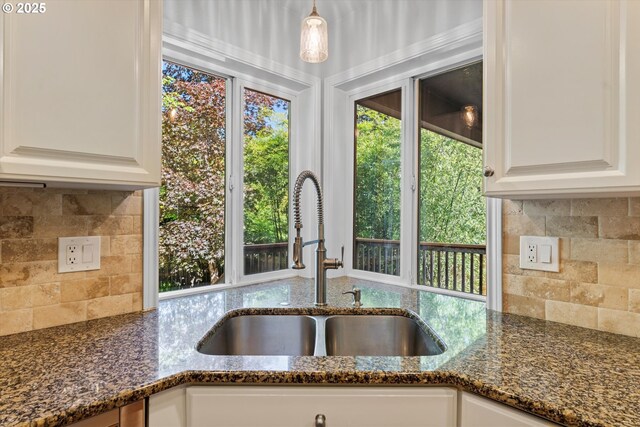 kitchen with a sink, dark stone counters, backsplash, and white cabinets