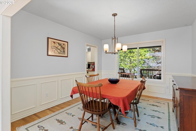 dining space featuring light wood-style flooring, a chandelier, wainscoting, and a decorative wall