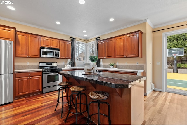 kitchen with appliances with stainless steel finishes, brown cabinets, light wood-style flooring, and a kitchen breakfast bar