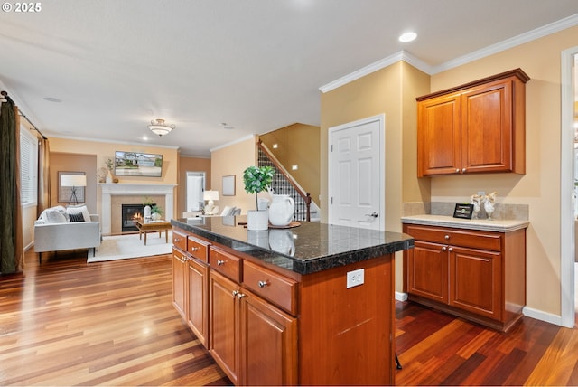kitchen featuring dark wood finished floors, ornamental molding, a center island, brown cabinetry, and a glass covered fireplace