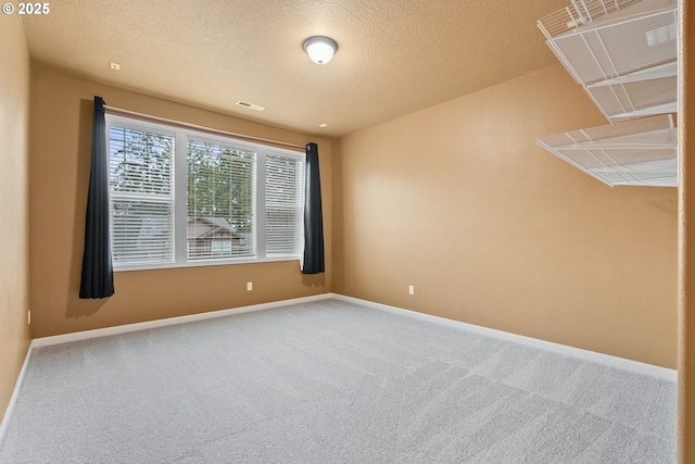 carpeted empty room featuring a textured ceiling, visible vents, and baseboards