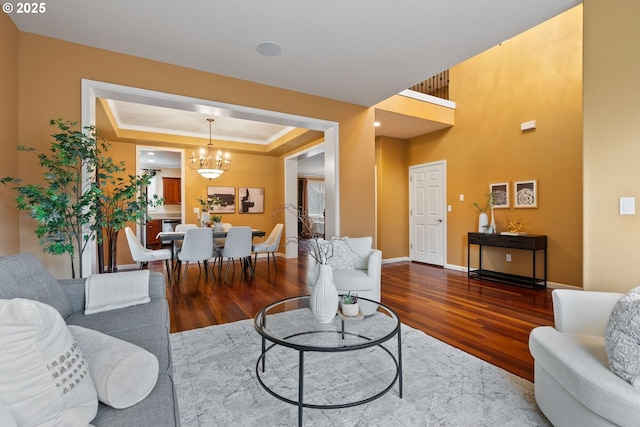 living area featuring a chandelier, wood finished floors, baseboards, a raised ceiling, and crown molding