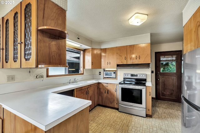 kitchen with appliances with stainless steel finishes, a peninsula, light countertops, under cabinet range hood, and a sink