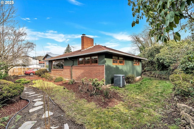 view of side of property with central AC unit, stucco siding, a chimney, fence, and brick siding