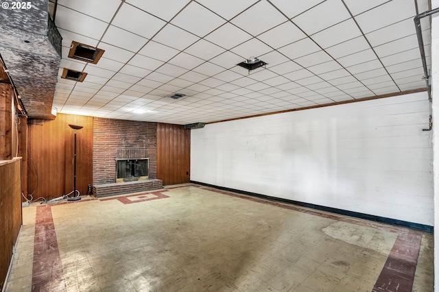 finished below grade area with wood walls, visible vents, baseboards, a brick fireplace, and tile patterned floors