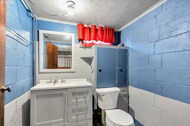 bathroom featuring concrete block wall, vanity, and toilet