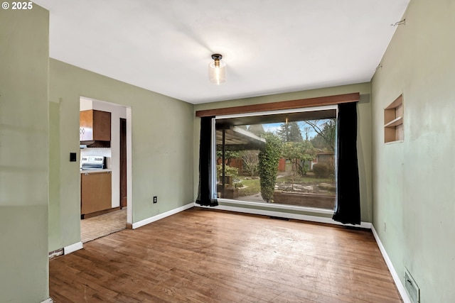 empty room featuring wood finished floors, visible vents, and baseboards