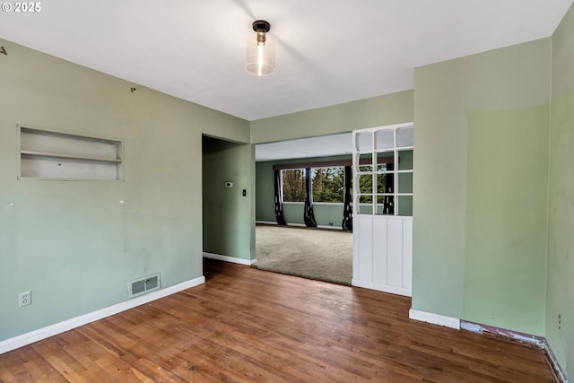 spare room featuring wood finished floors, visible vents, and baseboards