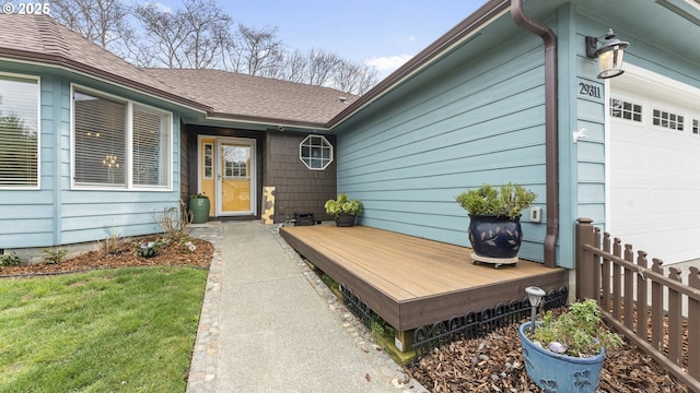 entrance to property with roof with shingles, a yard, fence, a deck, and a garage