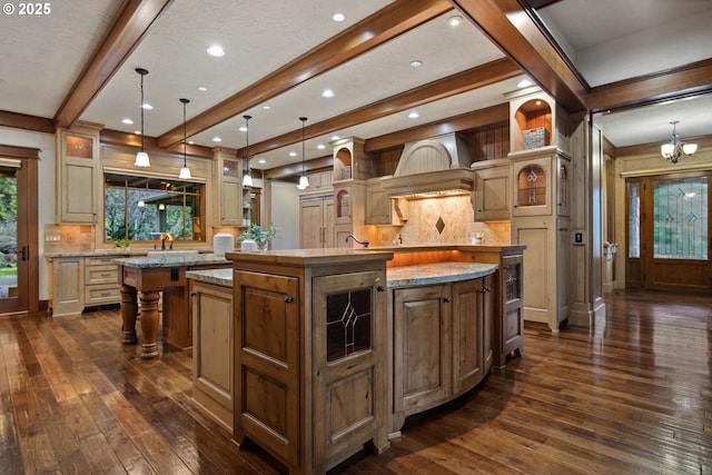 kitchen with pendant lighting, decorative backsplash, dark wood-type flooring, a center island with sink, and an inviting chandelier