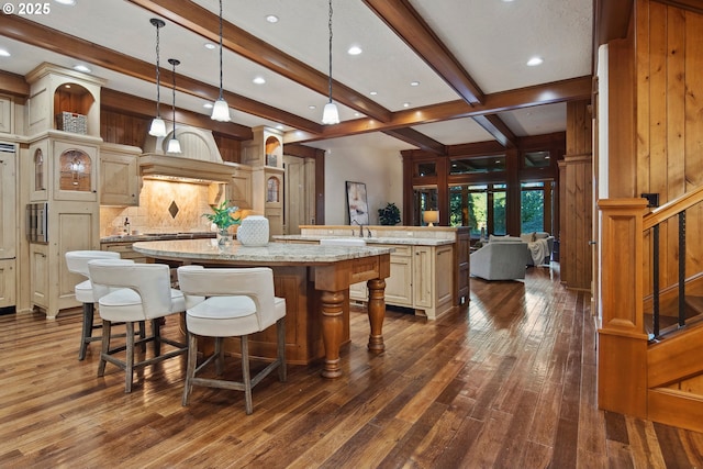 kitchen with hanging light fixtures, a kitchen breakfast bar, light stone counters, a center island with sink, and cream cabinetry