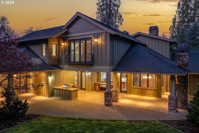 back house at dusk featuring a balcony and a patio area