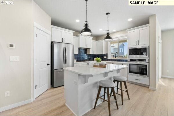 kitchen featuring a center island, white cabinets, decorative backsplash, appliances with stainless steel finishes, and a kitchen bar