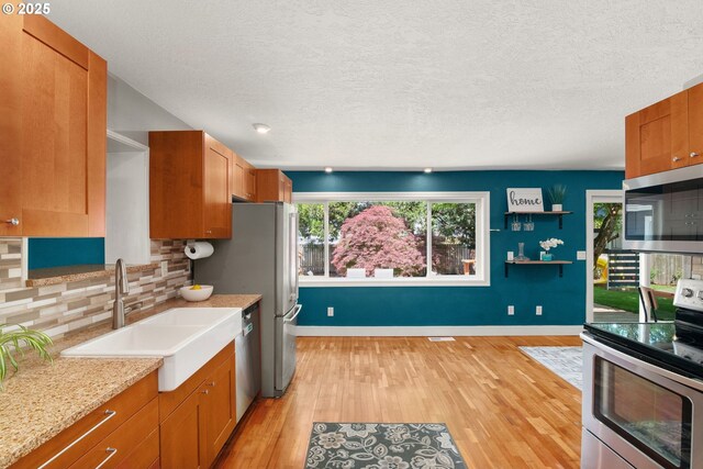 kitchen with stainless steel appliances, light wood-style flooring, tasteful backsplash, a sink, and brown cabinets