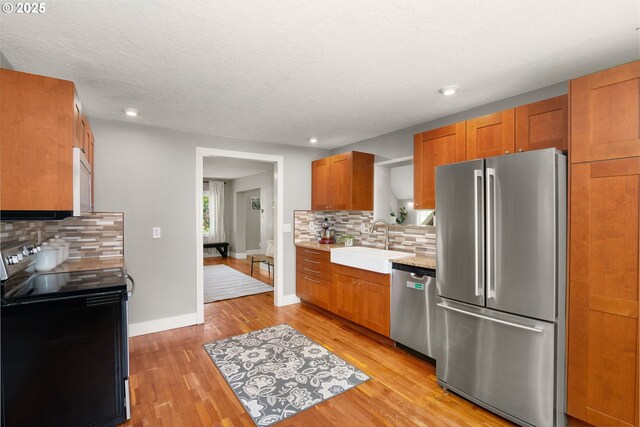 kitchen featuring appliances with stainless steel finishes, a sink, light countertops, backsplash, and light wood-style floors
