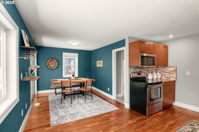 kitchen with appliances with stainless steel finishes, wood finished floors, decorative backsplash, baseboards, and a textured ceiling