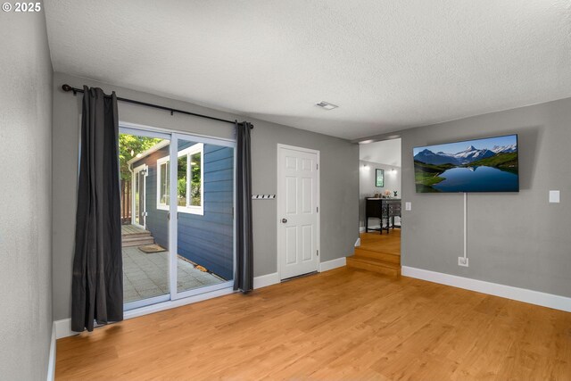 unfurnished living room featuring a textured ceiling, light wood-type flooring, and baseboards