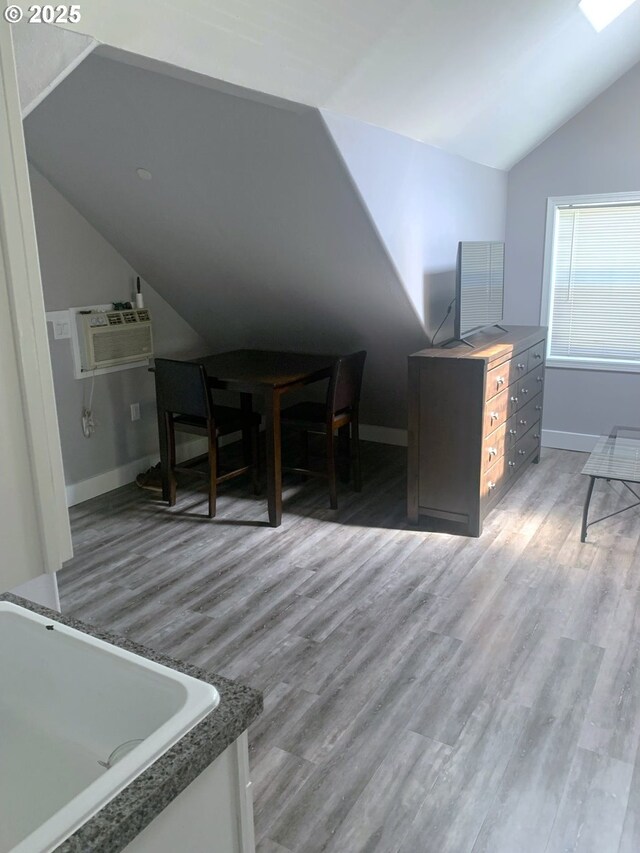 additional living space featuring lofted ceiling, a wall mounted AC, wood finished floors, and baseboards