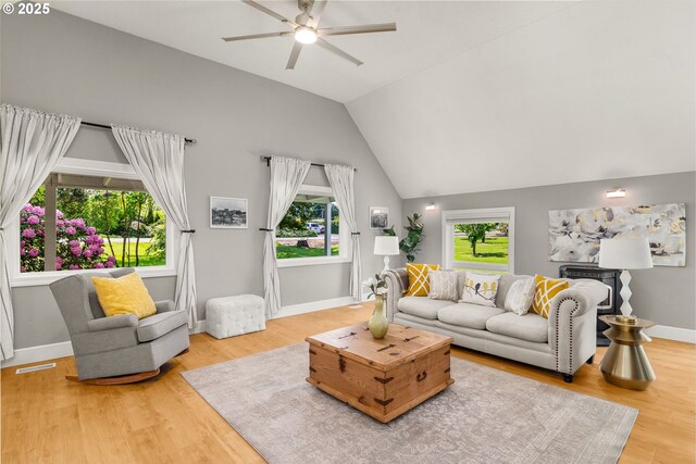 living room with ceiling fan, plenty of natural light, wood finished floors, baseboards, and vaulted ceiling