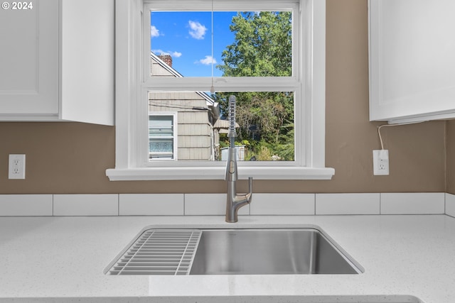 interior details featuring a sink, light stone countertops, and white cabinets