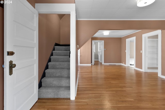 foyer entrance featuring light wood finished floors, stairway, baseboards, and ornamental molding