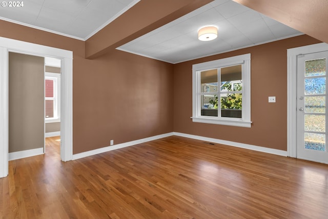 spare room with baseboards, wood finished floors, visible vents, and ornamental molding