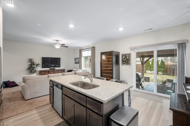 kitchen featuring sink, light stone counters, light hardwood / wood-style flooring, stainless steel dishwasher, and an island with sink