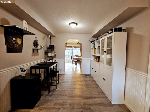 corridor featuring a wainscoted wall, arched walkways, and a textured ceiling