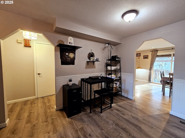 dining space featuring a textured ceiling, wood finished floors, arched walkways, and wainscoting