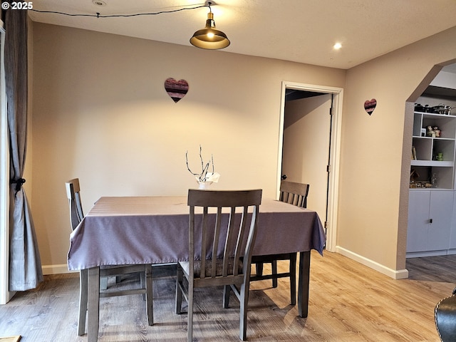 dining area featuring arched walkways, light wood-type flooring, and baseboards