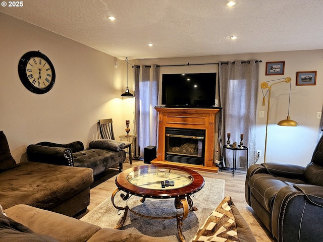 living area with light wood-type flooring, a textured ceiling, and a glass covered fireplace