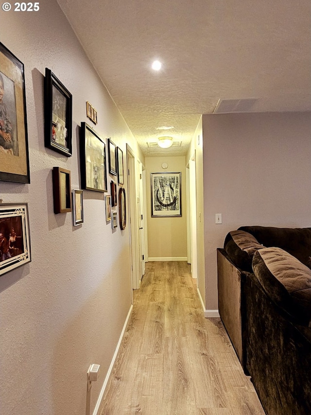 hall featuring a textured ceiling, baseboards, and light wood-style floors