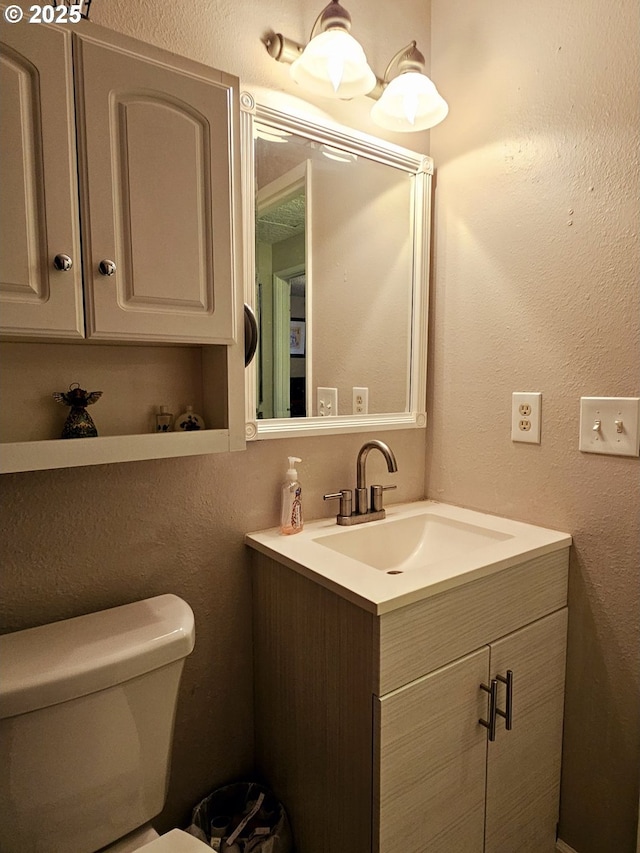 bathroom featuring toilet, vanity, and a textured wall